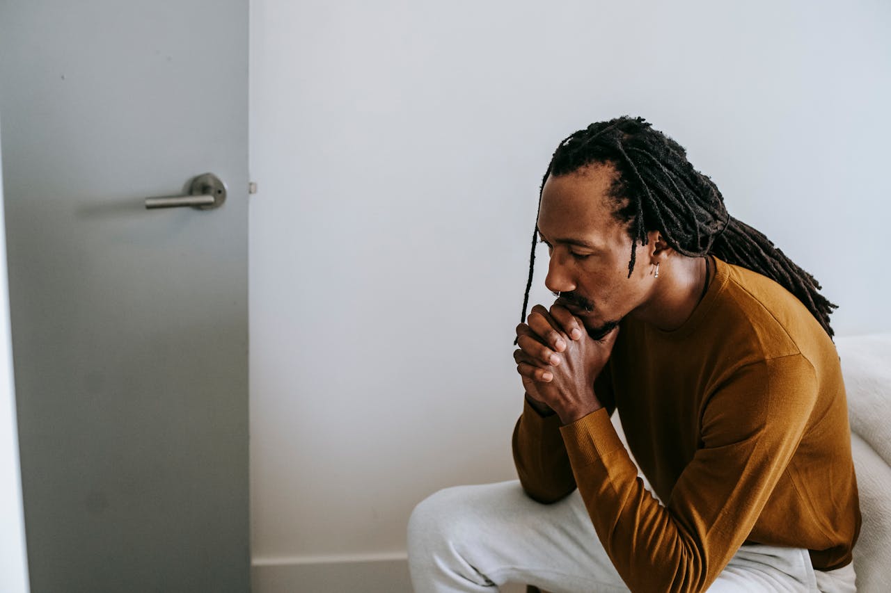 our-services-03 Young man with dreadlocks sits pensively indoors, capturing a moment of thoughtful introspection.